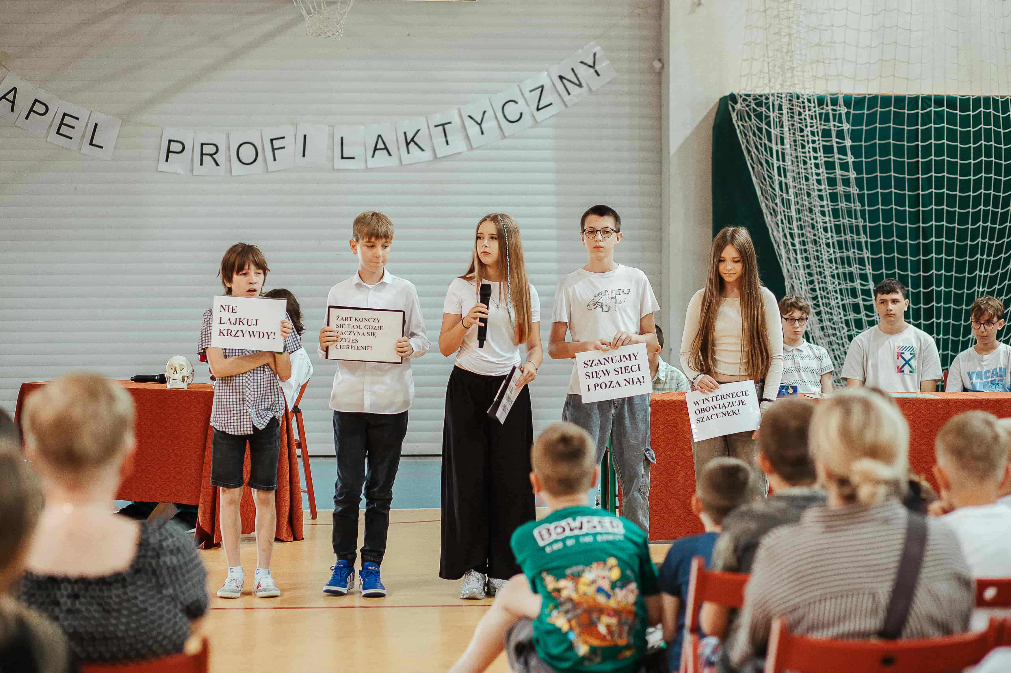 Uczniowie podczas przedstawienia prezentują kartki z hasłami dotyczącymi higieny cyfrowej i bezpiecznego korzystania z internetu