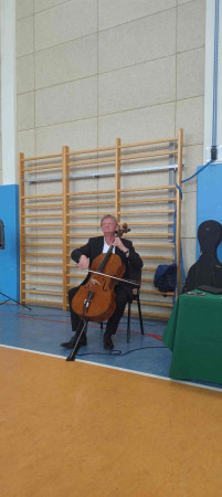 Muzyk gra na instrumencie przed uczniami podczas koncertu ‘Smyczkowanie na śniadanie’, zdjęcie 2 z 3