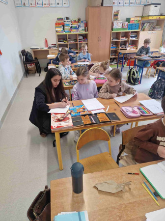 Uczniowie siedzący podczas prezentacji o Gruzji – widoczny wolontariusz i dzieci, zdjęcie 1 z 5