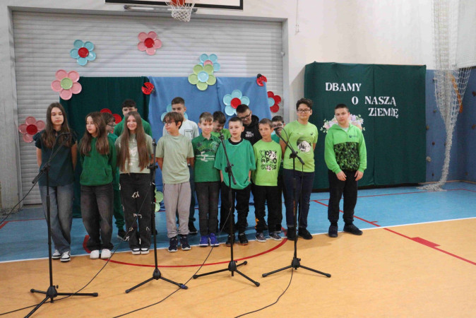 Dzieci w zielonych strojach śpiewają na scenie podczas szkolnego festiwalu ekologicznego, zdjęcie 3 z 5