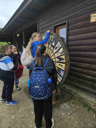 Uczniowie kręcą drewnianym kołem edukacyjnym przy budynku podczas wycieczki w Góry Świętokrzyskie, zdjęcie 2 z 5