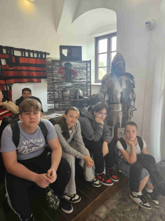 Czterech uczniów siedzi obok zbroi rycerskiej i historycznych rekwizytów podczas szkolnej wycieczki w Góry Świętokrzyskie, zdjęcie 3 z 5