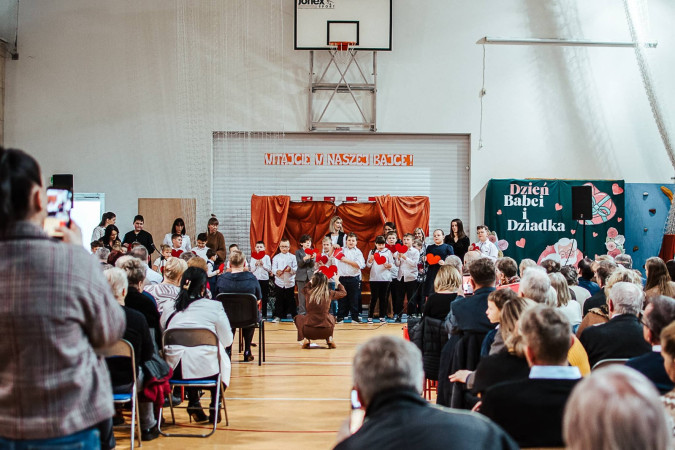 Dzieci występujące trzymają serca, stojąc na akademii z okazji Dnia Babci i Dziadka, zdjęcie 4 z 5