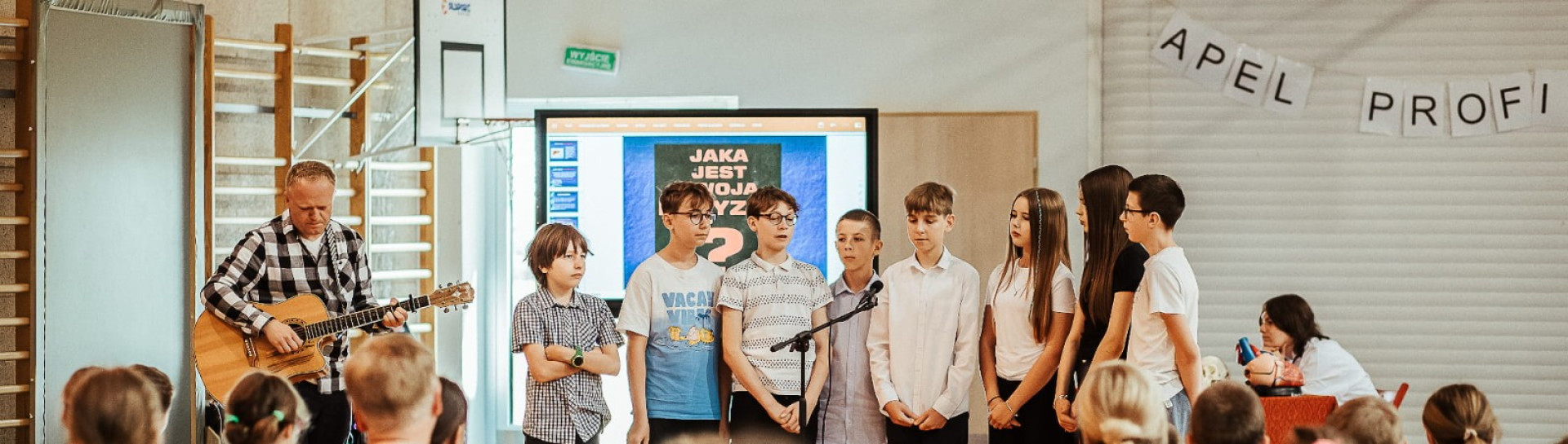 Uczniowie z nauczycielem wykonują utwór 'Tolerancja' podczas zakończenia apelu profilaktycznego