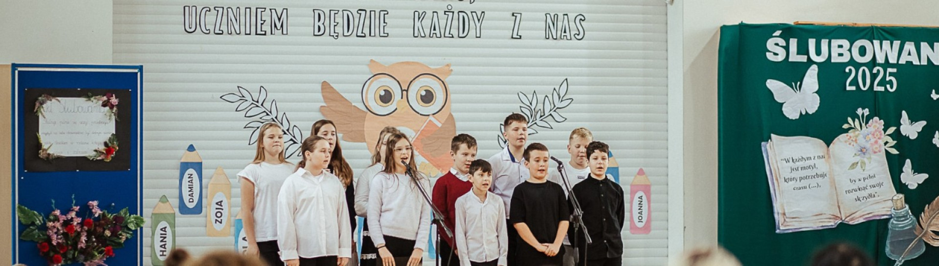 Dzieci z klas 0–5 śpiewają piosenkę dla nauczycieli na sali gimnastycznej