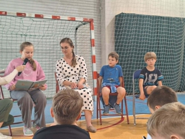 Uczennica czyta książkę kolegom i koleżankom na sali gimnastycznej, zdjęcie 1 z 5